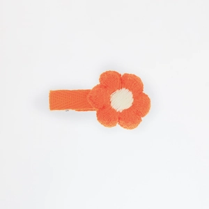 Detail of hand-knitted bright orange flower hair clip with cream center and fabric-wrapped pin
