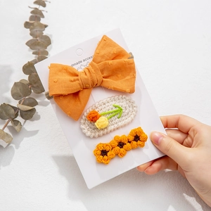 Close-up of handmade orange knit flower hair clips and bow set on white display card