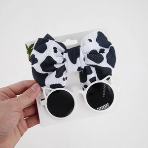 Detail view of cow print bow headband and white cat-ear sunglasses for infants