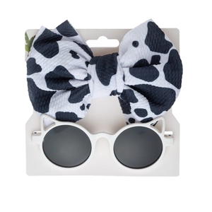 Detail of baby headband with cow pattern bow and cat ear sunglasses on a white card