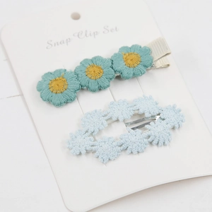 Detailed embroidery of blue daisy snap clips on a white presentation card