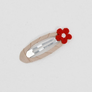 Detail einer Baby-Haarspange mit rot gesticktem Gänseblümchen auf beigem Ripsband