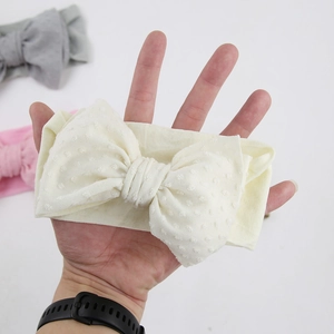 Détail d'un bandeau pour bébé en nylon souple avec un grand nœud à pois de couleur crème
