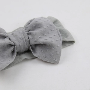 Détail d'un bandeau gris pour bébé avec un grand nœud et une texture jacquard à pois