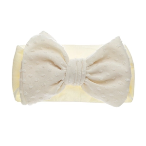 Gros plan d'un bandeau bébé en nylon beige avec un nœud doux à texture à pois suisses