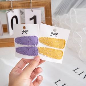 Handheld view of two sets of embroidered floral lace hair clips for kids in purple and yellow