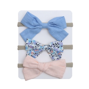 Detailed view of three baby bow headbands in sky blue, floral print, and soft pink