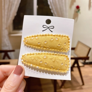 Detailed macro view of yellow cotton hair clips with white floral embroidery and scallop edges