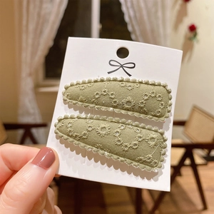 Detailed close-up of olive green embroidered daisy fabric hair clips for kids on card