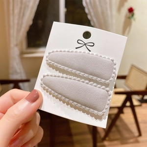 Close-up of two beige lace fabric hair clips for kids on a white display card