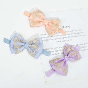 Detailed close-up of lace baby headbands in soft pink, blue, and purple with gold embroidery