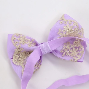 Close-up of baby lace bow headband with gold embroidery and purple elastic nylon band