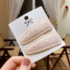 Detail of light pink fabric BB hair clips with grid stitching and pom-pom on display card