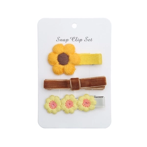 Vue détaillée des barrettes à fleurs brodées et du nœud en velours sur support blanc