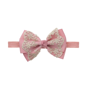 Detail showing pink tiered bow with beige lace embroidery on a soft elastic baby headband