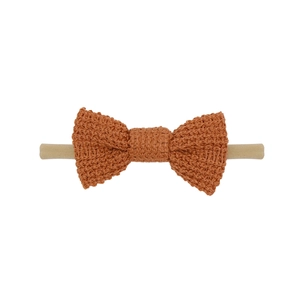 Close-up of rust red knitted cotton bow on a soft nude nylon headband for infants