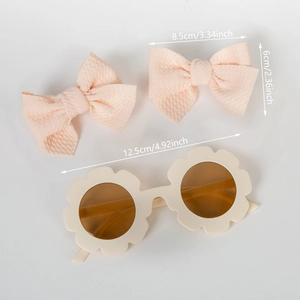 Vue à plat de lunettes de soleil fleurs pour enfants et deux barrettes nœuds rose clair