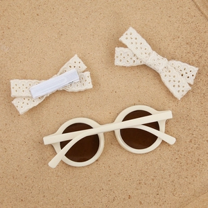 Détail de lunettes de soleil enfant rondes crème et pinces à cheveux en dentelle assorties
