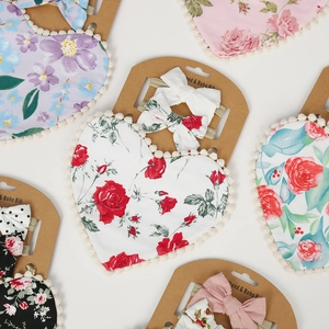 Flat lay of baby cotton bib with pom-pom trim and matching bow headband on display card