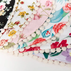 Close-up of floral printed cotton baby bibs with white pom-pom fringe edging details