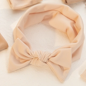 Macro detail of soft ribbed knit fabric texture on a peach infant bow headband