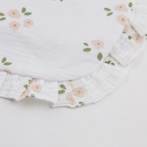 Detail of baby muslin cotton bib with delicate pink floral print and ruffled edges