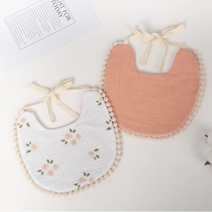 Detailed view of floral cotton baby bibs with delicate pom-pom lace trim and lace-up straps