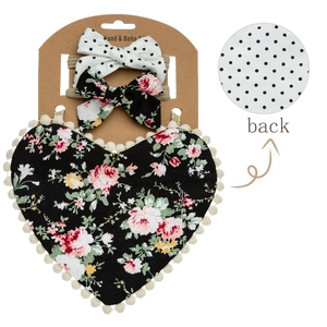 Detail of floral baby bib with fringe balls and matching bow headbands set on white back