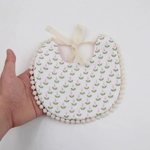 Close-up of baby floral bib with pink tulip pattern and delicate cream lace trim detailing