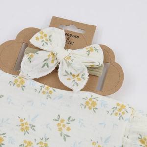 Close-up of white cotton gauze bib and headband with yellow floral pattern on a card