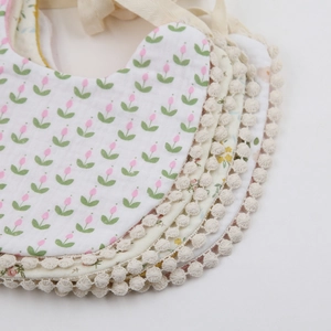 Detail of stacked cotton baby bibs with floral prints and white lace trim edges