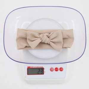Detailed view of beige ribbed knit baby bow headband weighing 23g on a scale