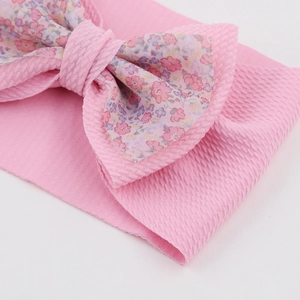 Close-up of baby headband showing pink ribbed knit fabric and floral print bow details