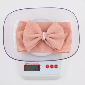 Pink rib fabric baby headband with pearl-encrusted bow accent shown on a digital scale