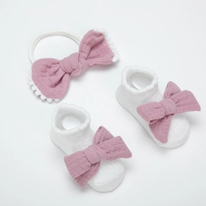 Detail von weißen Baby-Spitzensocken und einem altrosa Stirnband-Set mit Schleifen