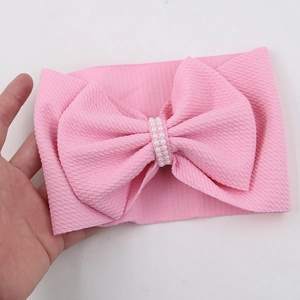 Detail of pink knit baby headband featuring a large bow with four rows of white pearls