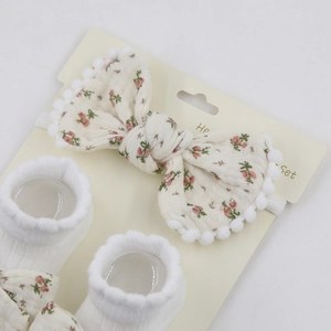 Detailansicht von Baby-Stirnband und Socken-Set mit rosa Blumenmuster und Bommel-Dekor
