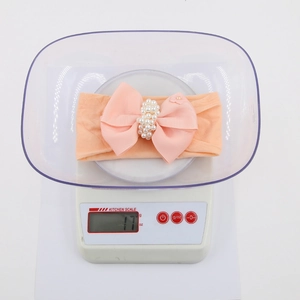 Bandeau bébé rose avec grand nœud perlé pesant 17g sur une balance de cuisine blanche