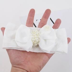 Détail d'un bandeau blanc pour bébé avec un grand nœud en gros-grain et perles