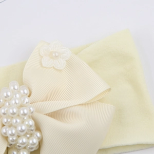 Détail d'un bandeau bébé avec nœud en gros-grain blanc, perles et petite fleur en tissu