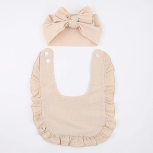 Close-up of beige baby bib with ruffle edges and ribbed headband with bow detail