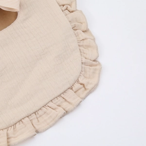Detailed macro view of ruffled cotton muslin baby bib in soft beige with fine stitching