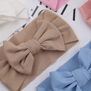 Flat lay of colorful ribbed baby headbands with large bows on a clean white background