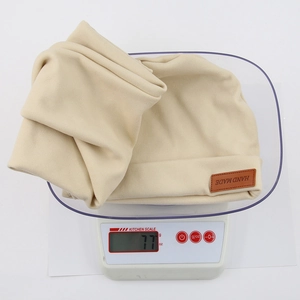 Beige baby knit hat and neck warmer scarf set weighing 77g on a digital scale