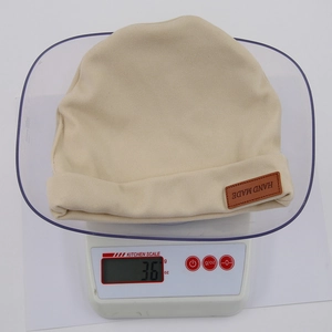 Detail of beige knit baby hat showing handmade leather label and 36g product weight