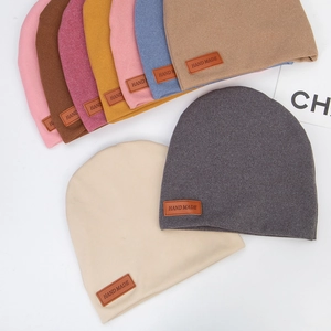 Flat lay of soft double-layer baby knit hats in multiple colors with handmade faux leather tags