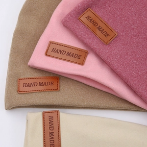 Detail of knitted baby hats in four colors featuring handmade embossed leather labels