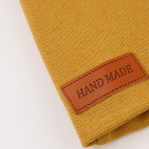 Detailed macro view of yellow baby hat featuring a brown leather Hand Made tag