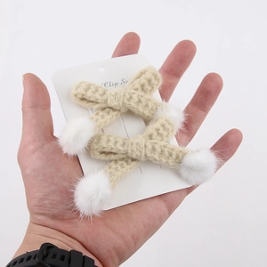 Vue détaillée de pinces à cheveux nuds beige au crochet avec pompons en fausse fourrure blanche