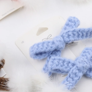 Détail de pinces à cheveux avec nœud en tricot bleu clair et décorations de plumes blanches